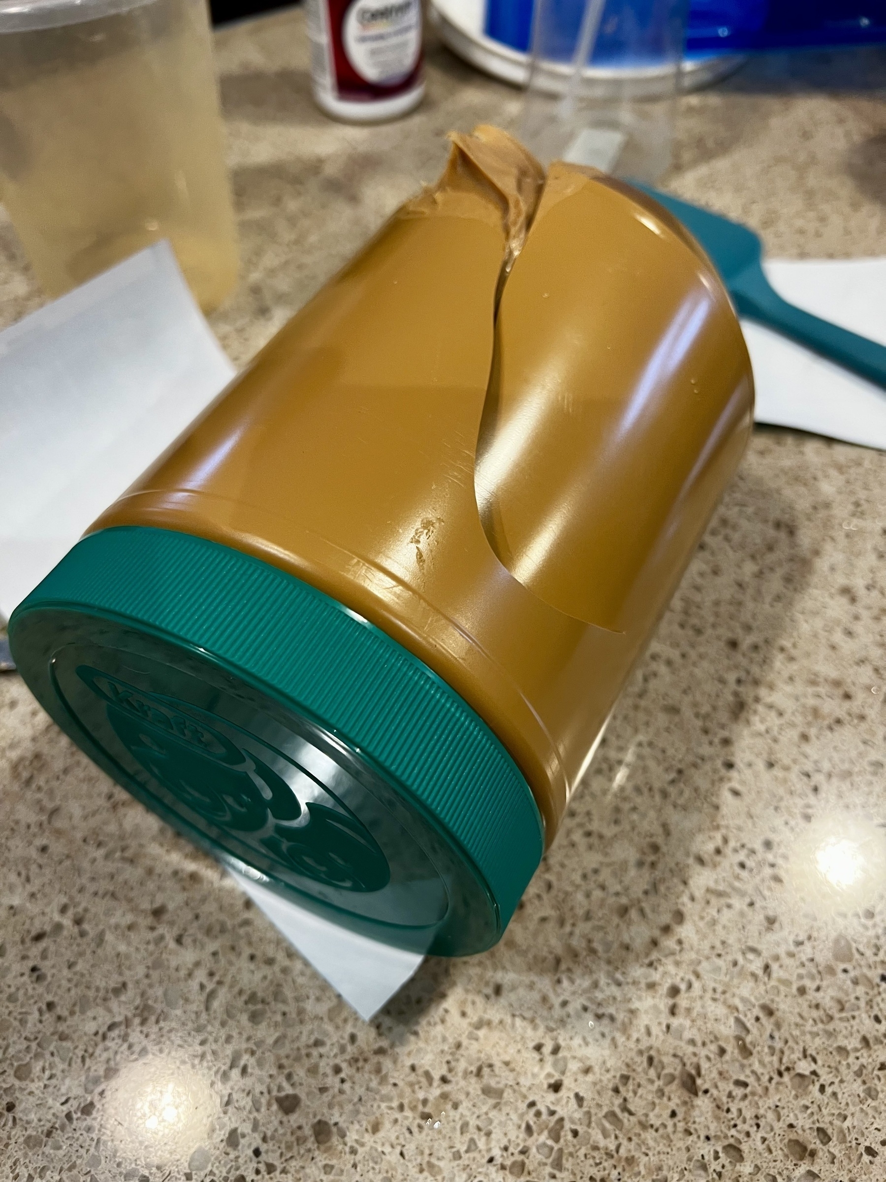 A peanut butter container sits on a counter with a large crack in it. 