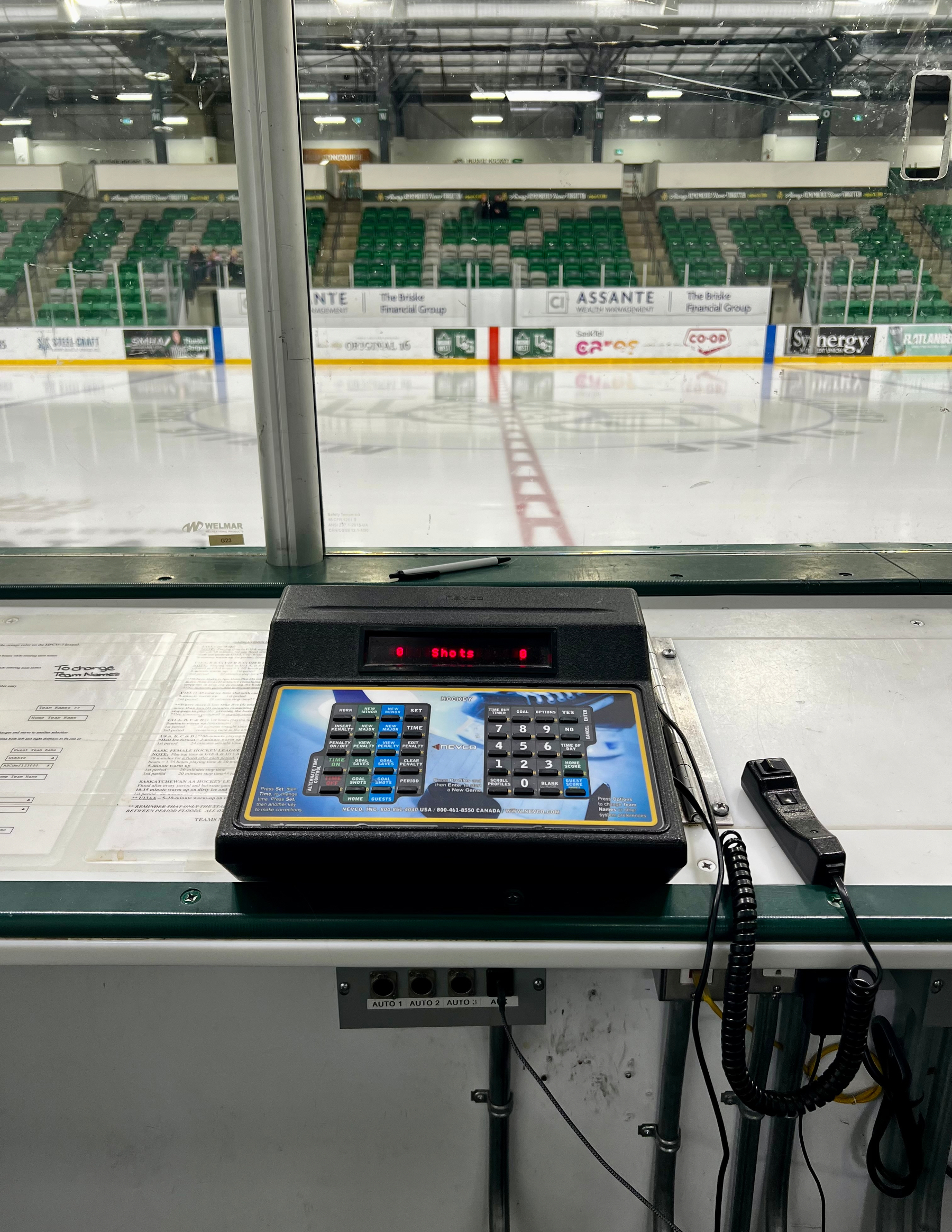 A control panel with buttons and a telephone is positioned at an ice hockey rink, viewed from inside a booth.