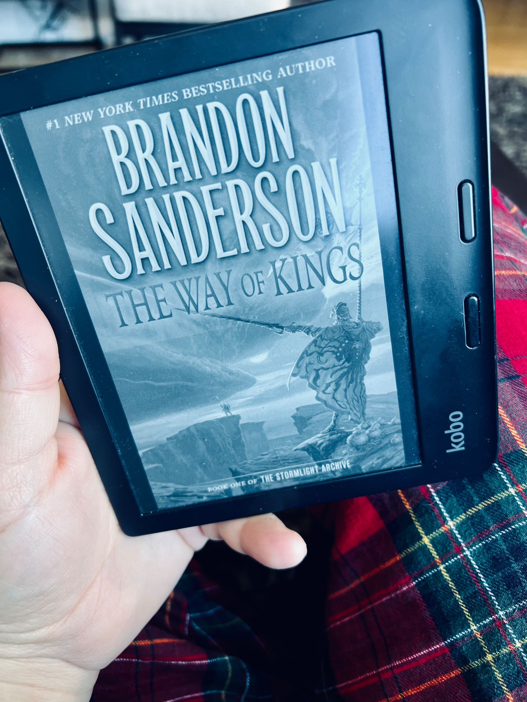 A hand is holding an e-reader displaying the cover of The Way of Kings by Brandon Sanderson.